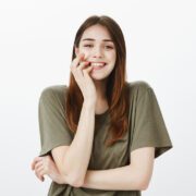 Studio shot of grinning attractive european woman in casual t-shirt, biting finger sensually, feeling temptation and happiness while taking part in curious event, standing over gray background Pijat Refleksi Palembang