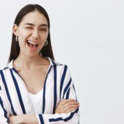 If you know what I mean. Confident and flirty cute woman in striped blouse, winking joyfully at camera, smiling broadly and holding hands crossed on chest in self-assured pose, hinting at something Tempat Pijat Plus Bandung