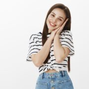 Time to rest and get health sleep. Portrait of smart good-looking caucasian woman in trendy outfit, leaning face on hands and smiling broadly, feeling tired after long day, relaxing over white wall Panti Pijat Bandung